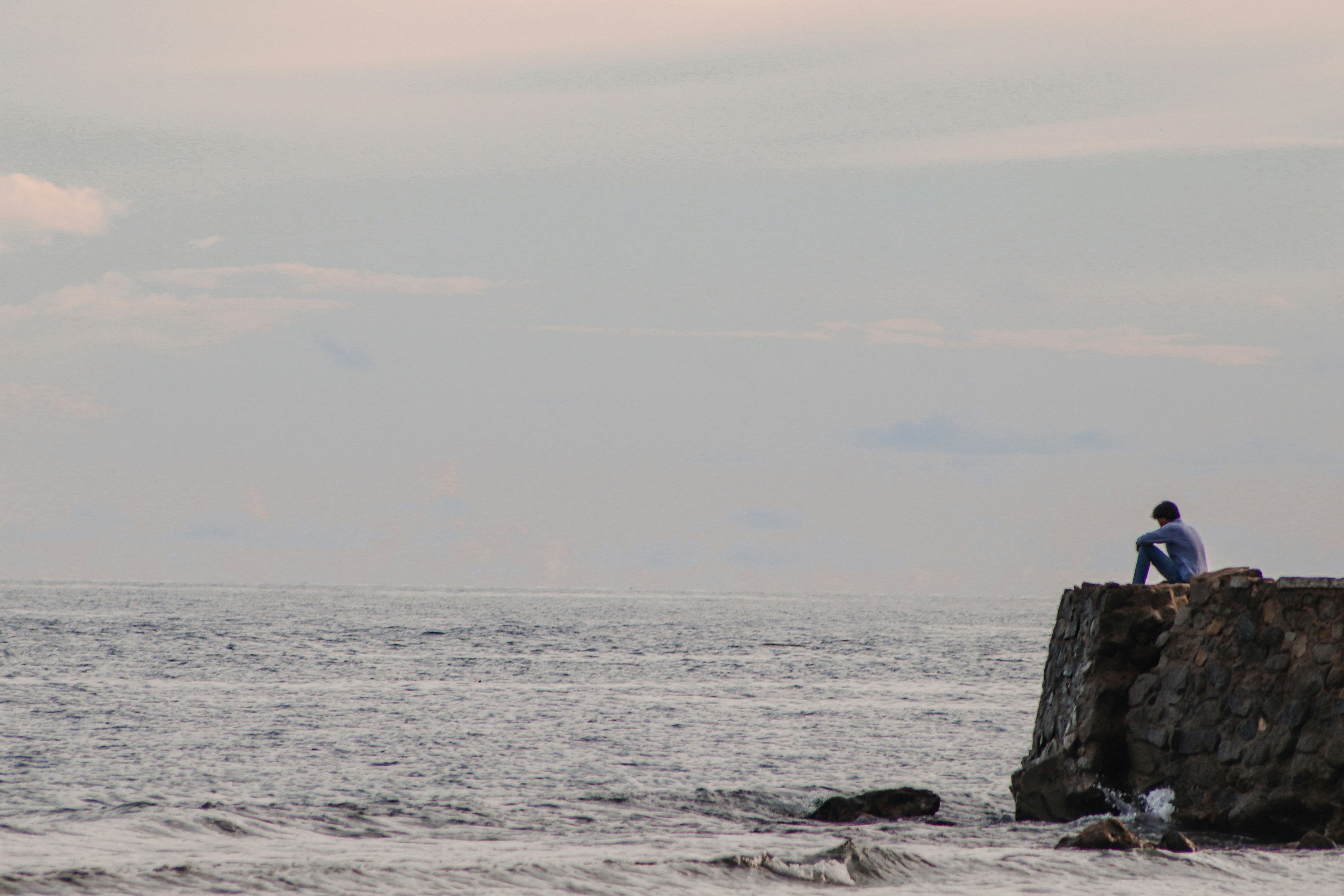 A stressed man sitting on a rock by the sea. His sex drive is low due to the stress.