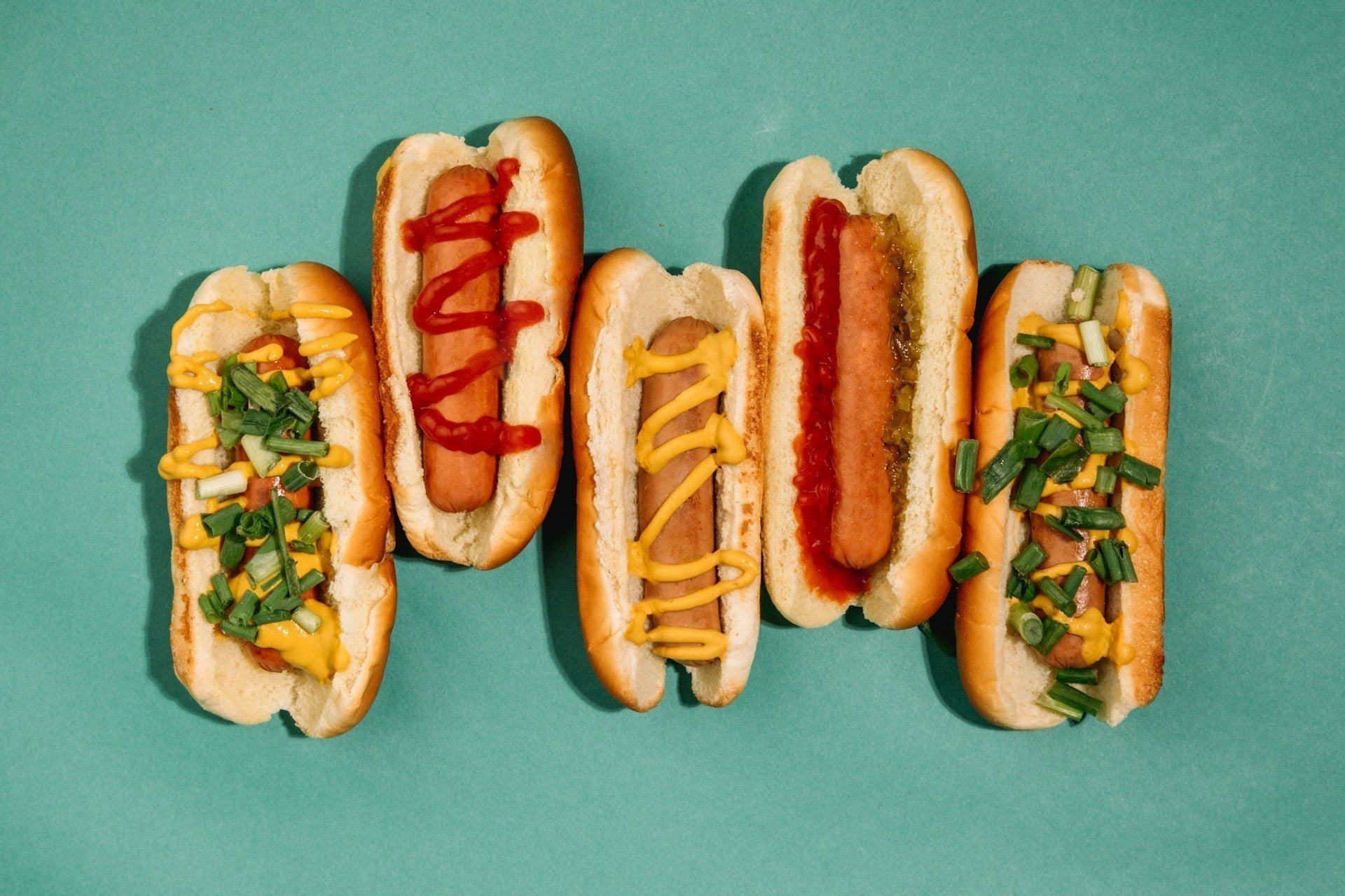five hot dogs of different sizes and toppings on a green background serving as a metaphor for grower vs shower